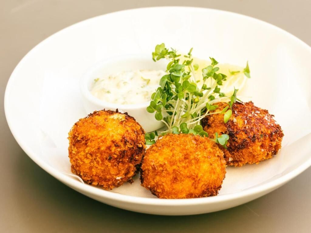 A plate with three breaded and fried items, a small bowl of white sauce, and some green garnish.