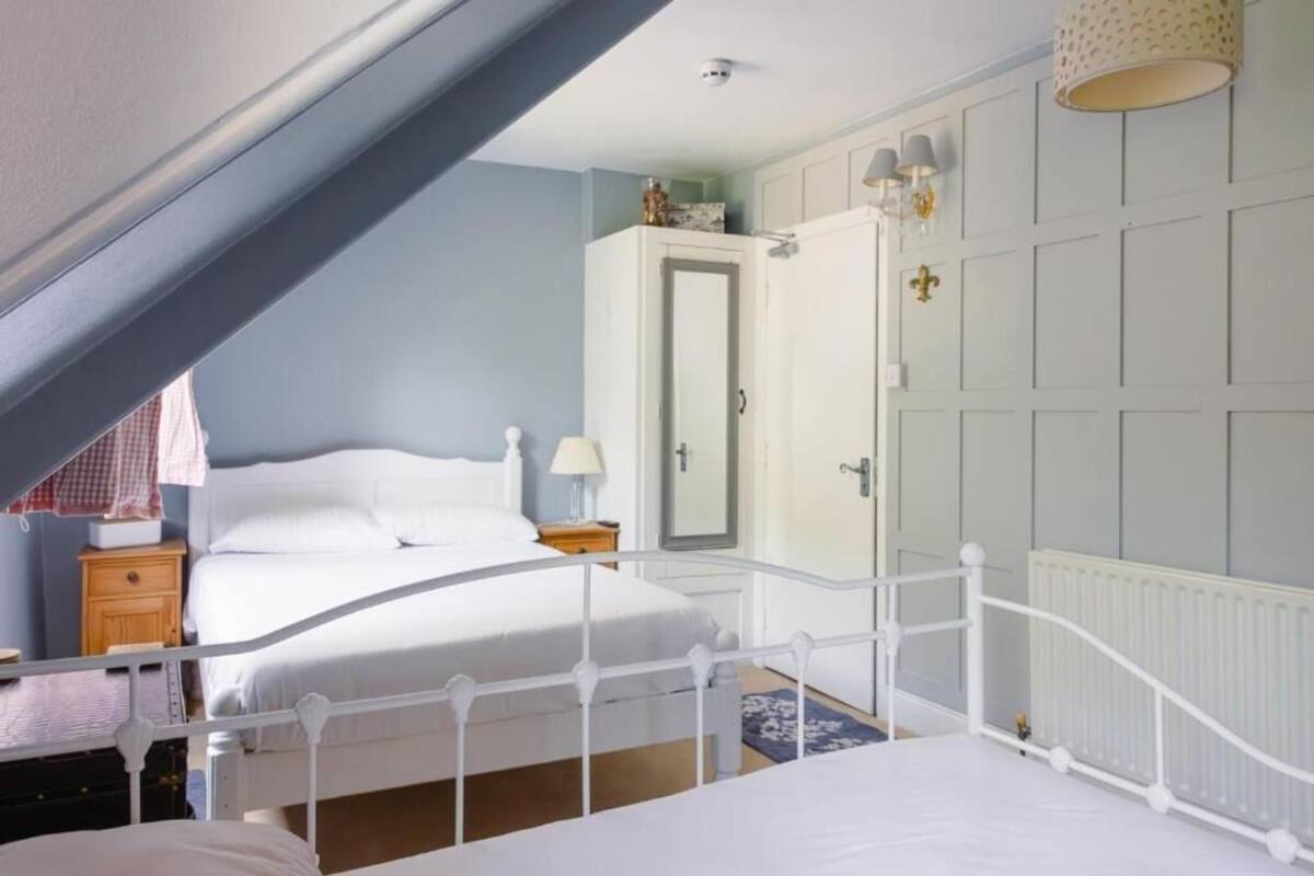 Un dormitorio con una cama blanca, una mesita de noche, un tocador y una puerta con espejo.