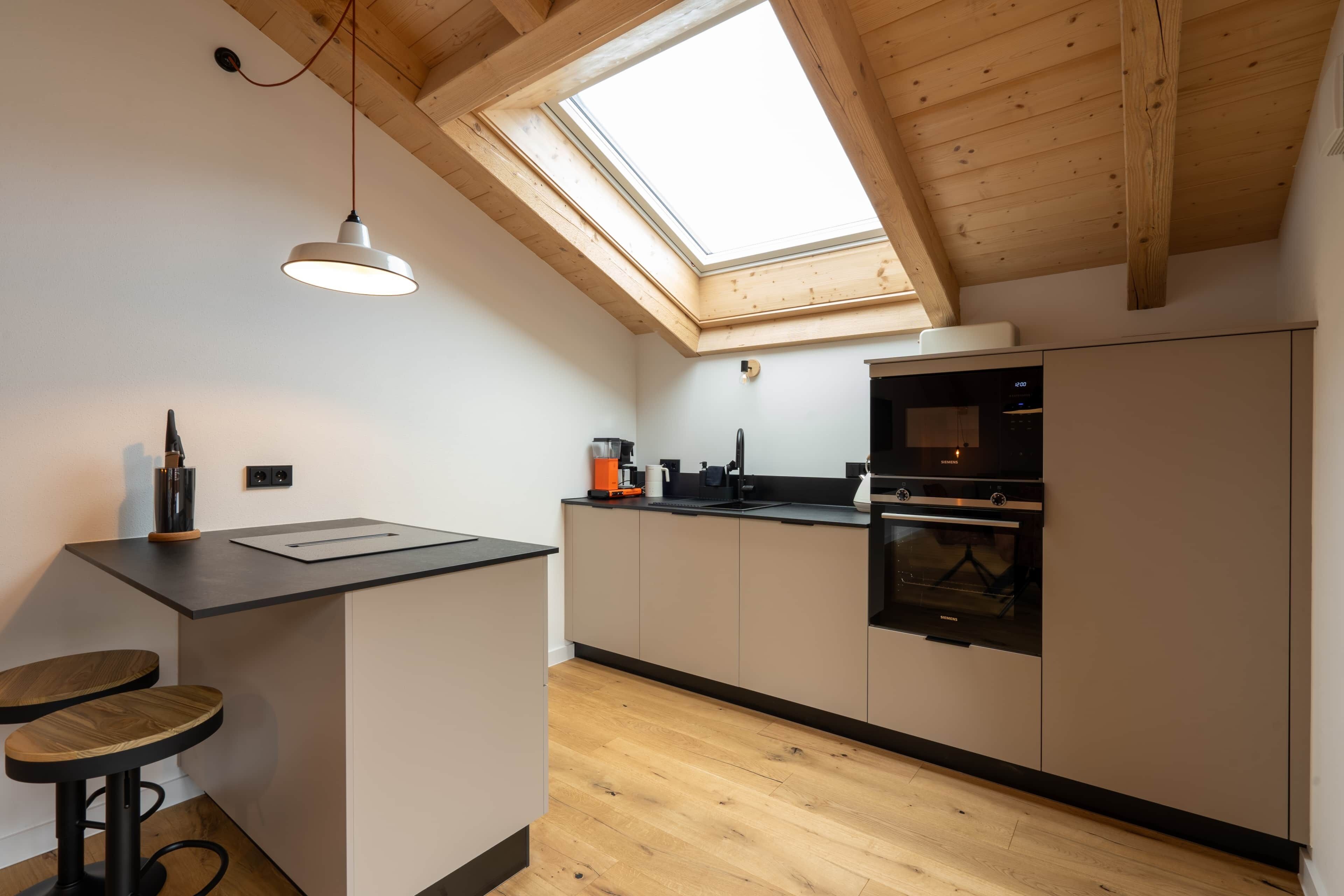 Una cocina moderna con tragaluces, vigas de madera y una isla central con taburetes.