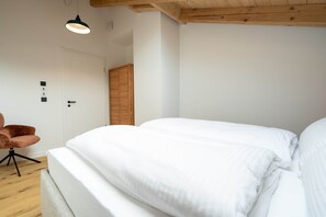 A bedroom with a large bed, a wooden ceiling, a white door, and a small chair.