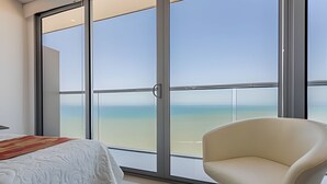 A hotel room with a large sliding glass door leading to a balcony with a view of the beach.