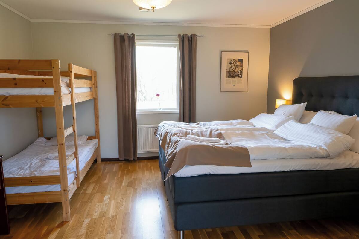 Una habitación con una cama nido, una cama individual, suelo de madera, una ventana con cortinas y un cuadro en la pared.