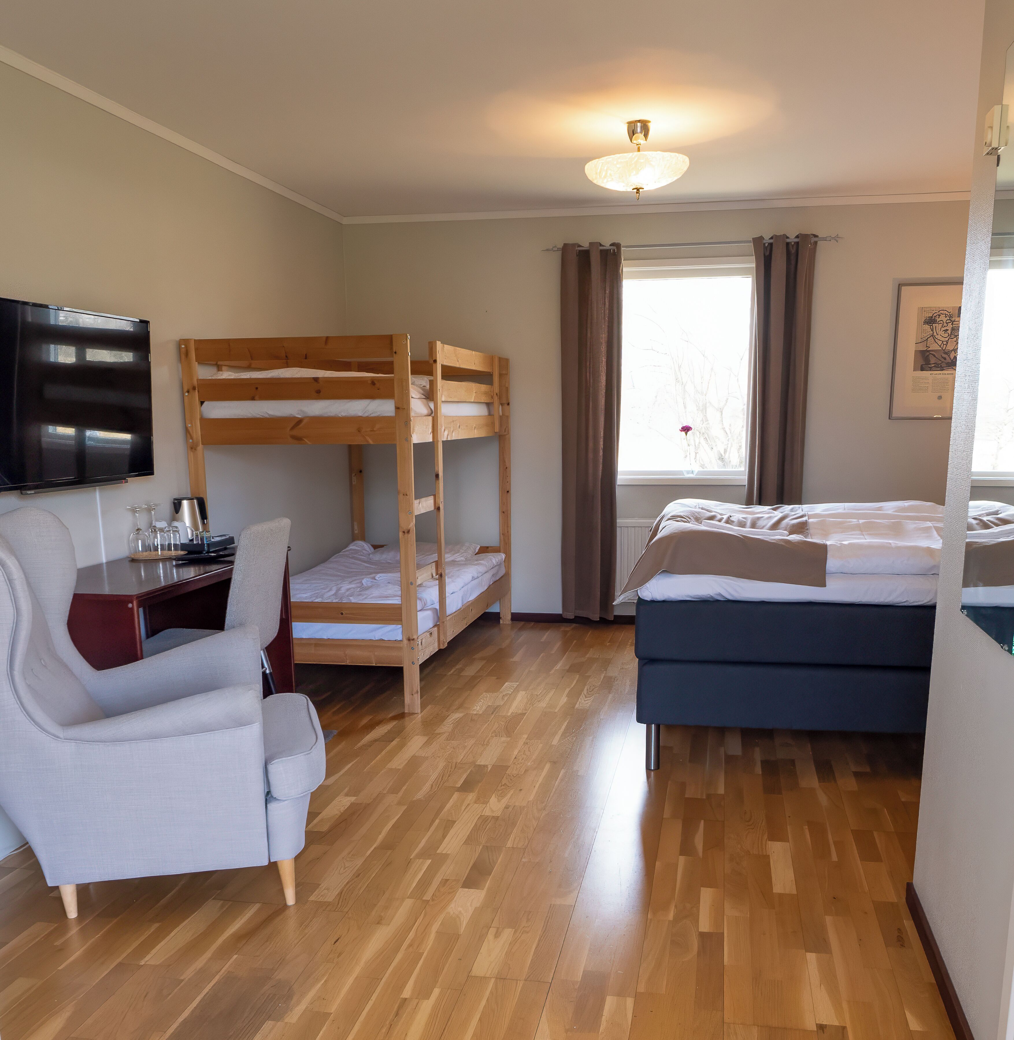 A room with a bunk bed, a desk with a chair, a television, and a bed.