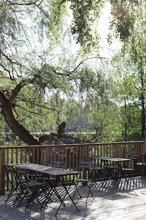 A wooden deck with tables and chairs, surrounded by trees. - Spångens Gästgivaregård (Ljungbyhed)