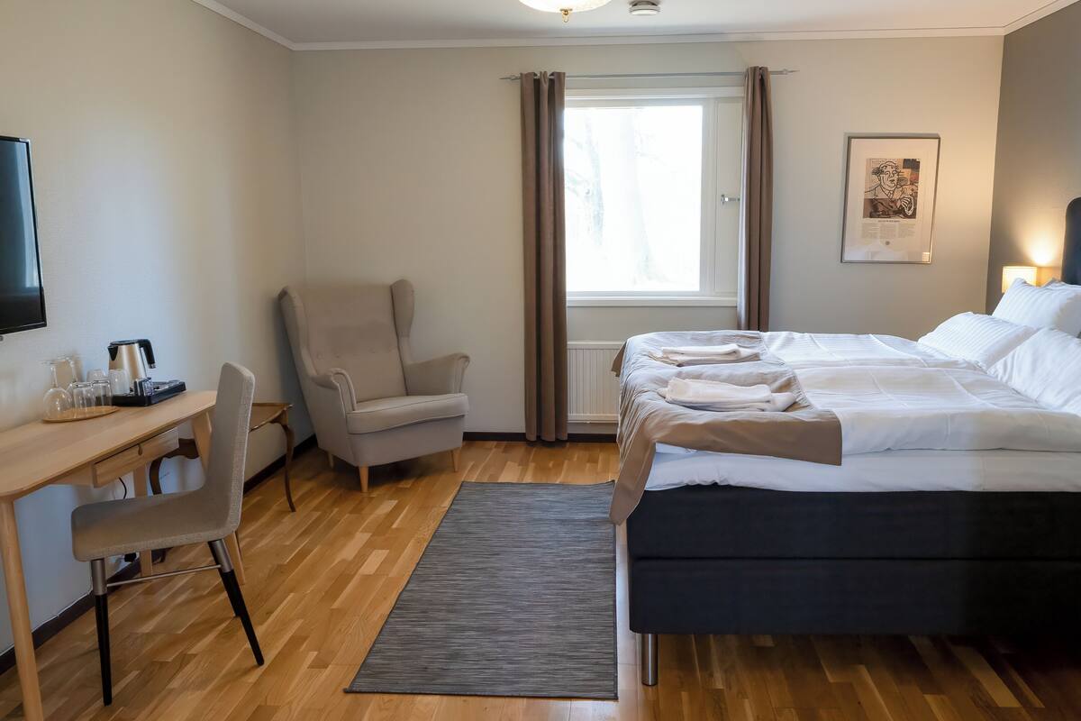 Una habitación de hotel con cama, escritorio con silla, cafetera y ventana con cortinas.
