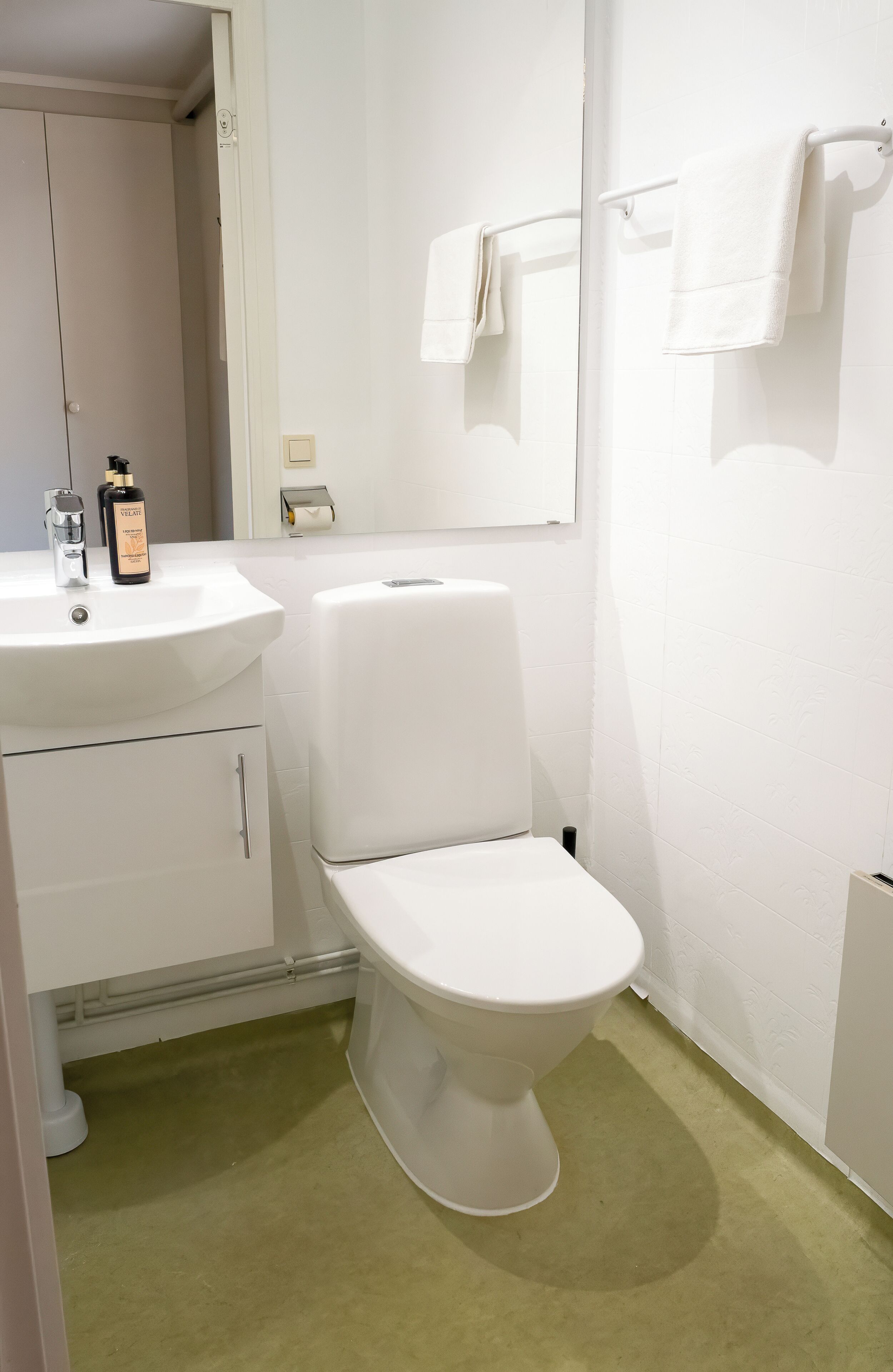Een kleine, schone badkamer met een wit wastafel, toilet en handdoekrek.