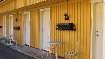 A row of yellow buildings with white doors, outdoor seating with metal tables and chairs, and a black lantern on the wall.