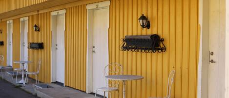 A row of yellow buildings with white doors, outdoor seating with metal tables and chairs, and a black lantern on the wall.