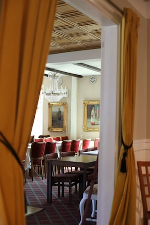 An interior dining area with a chandelier, red upholstered chairs, and framed artwork on the walls. - Spångens Gästgivaregård (Ljungbyhed)