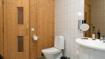 A bathroom with a wooden door, a toilet, a sink, a mirror, and a trash bin.