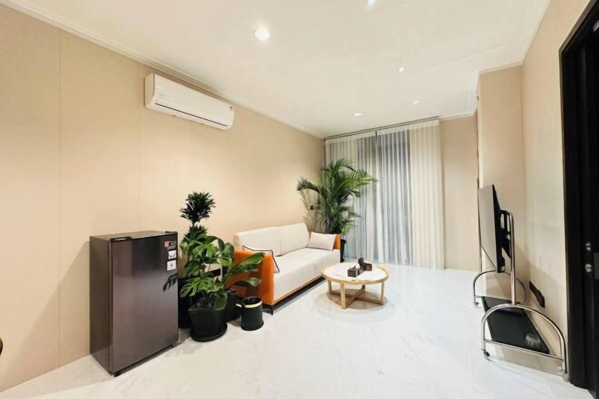 A modern living room with a sofa, a coffee table, a refrigerator, and potted plants.