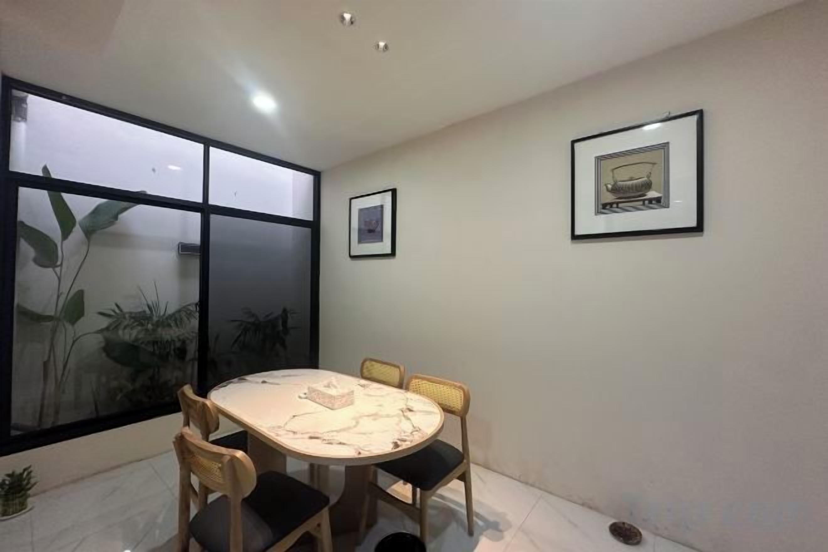 Een kamer met een ronde tafel, vier stoelen, een bloempot en twee ingelijste foto’s aan de muur.