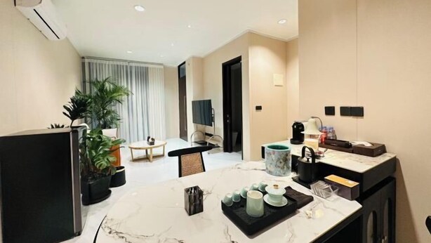 A modern hotel room with a marble dining table, a small kitchen area, a seating area with a TV, and a large window with curtains. - winner house (North Jakarta)