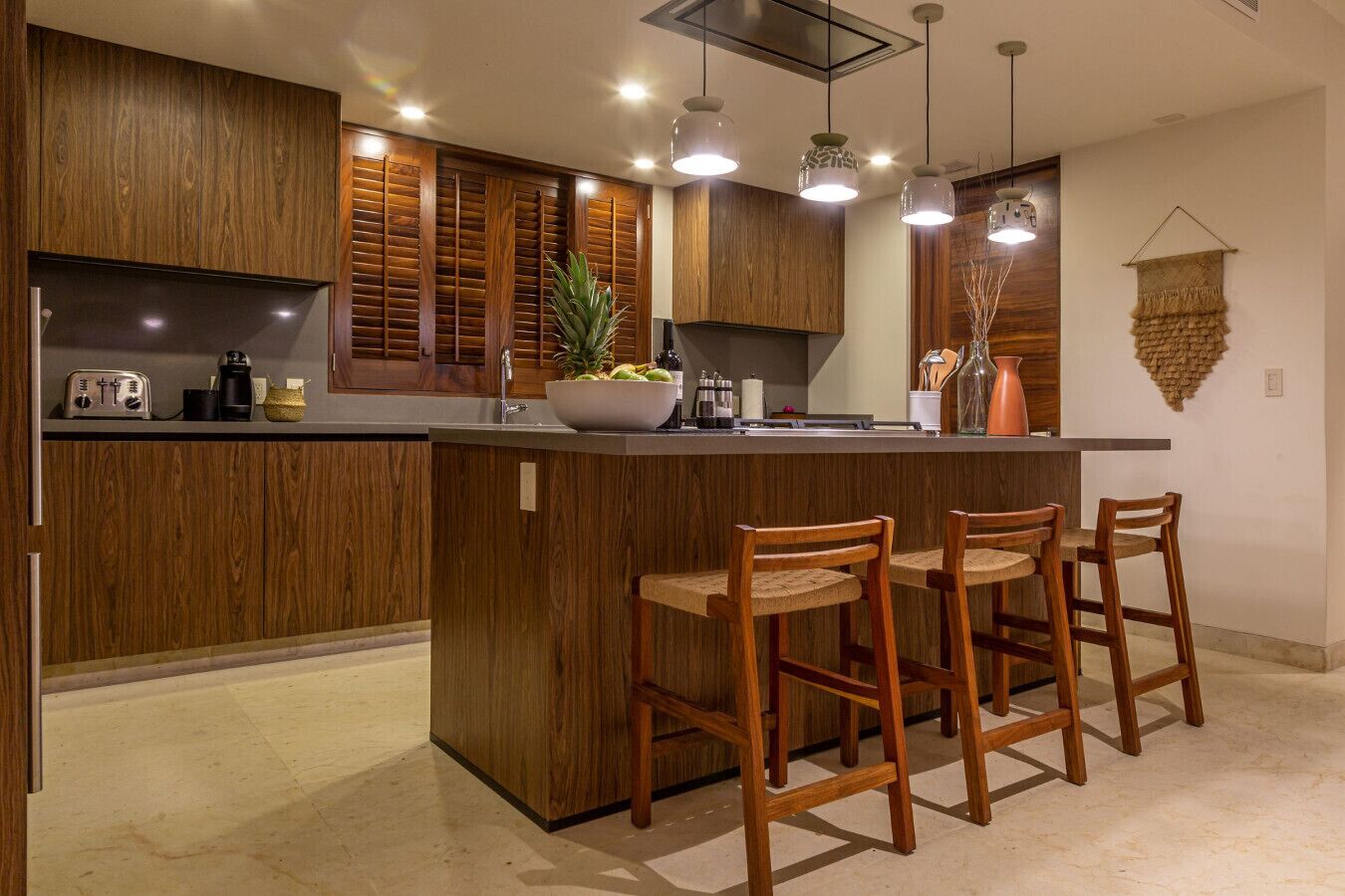 A modern kitchen with wooden cabinets, a central island with bar stools, and pendant lighting.