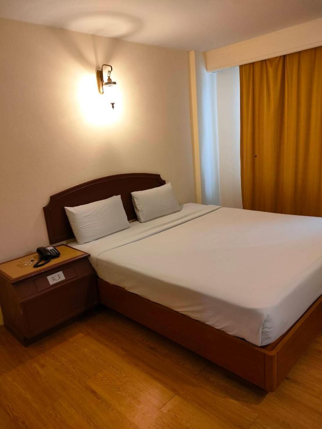 A hotel room with a single bed, a nightstand with a phone, and a wall-mounted light fixture.