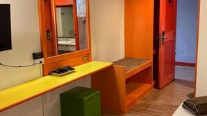 A compact hotel room with a wooden desk, a mirror, a green storage bin, and a red door. - INTERTOWER HOTEL (Su-ngai Kolok)