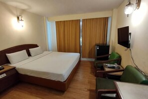 A hotel room with a bed, a desk, a chair, a TV, and a window with curtains. - INTERTOWER HOTEL (Su-ngai Kolok)