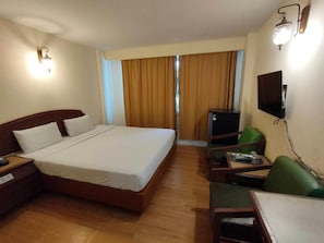 A hotel room with a bed, a desk, a chair, a television, and a window with curtains. - INTERTOWER HOTEL (Su-ngai Kolok)