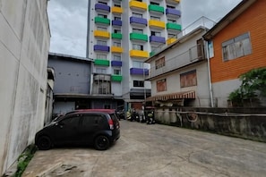 A narrow street with a parked car, a tall building with colorful balconies, and a building with a red and white facade.