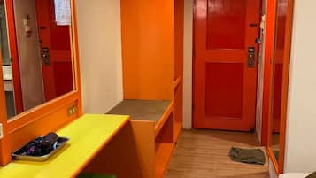 Um quarto com escrivaninha amarela, um banco verde, uma porta vermelha e um espelho.