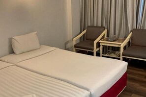 A hotel room with two beds, a small table with a chair, and a window with curtains. - INTERTOWER HOTEL (Su-ngai Kolok)