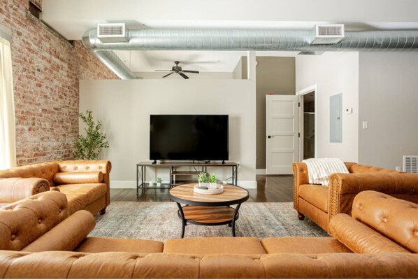 A living room with a large flat-screen TV, leather sofas, a coffee table, and a brick wall.