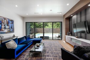 A modern living room with a blue sectional sofa, a glass coffee table, and a large TV mounted on a textured wall.