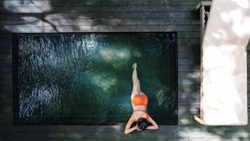 Una persona recostada en una cubierta de madera junto a una piscina rectangular con superficie de agua oscura.