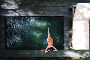 Una persona recostada en una cubierta de madera junto a una piscina rectangular con superficie de agua oscura.