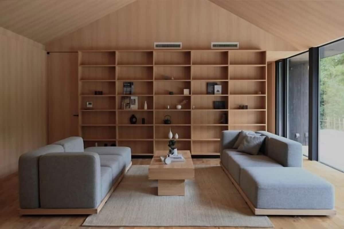 Ein modernes Wohnzimmer mit eingebauten Holzbögen, zwei grauen Sofas, einem Couchtisch und großen Fenstern.