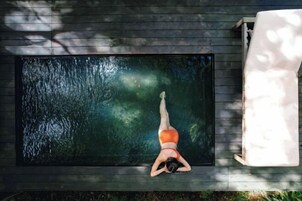 Una persona recostada sobre una plataforma flotante en una piscina rectangular rodeada por una terraza de madera.
