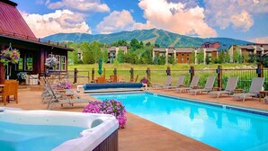 A swimming pool with lounge chairs and a hot tub, surrounded by a fence and mountains in the background. - Spacious 4BR home in Steamboat Springs, perfect for family getaways! (Steamboat Springs)