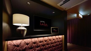 A hotel reception area with a tufted leather headboard, a wall-mounted TV, and a framed sign above it. - Hotel LALA kitashiga (Nagoya)