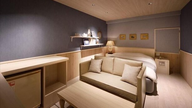 A compact hotel room with a bed, a sofa, a desk, and a small shelf with decorative items. - Hotel LALA kitashiga (Nagoya)