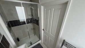 A modern bathroom with a glass-enclosed shower, a sink, and a door with paneling.