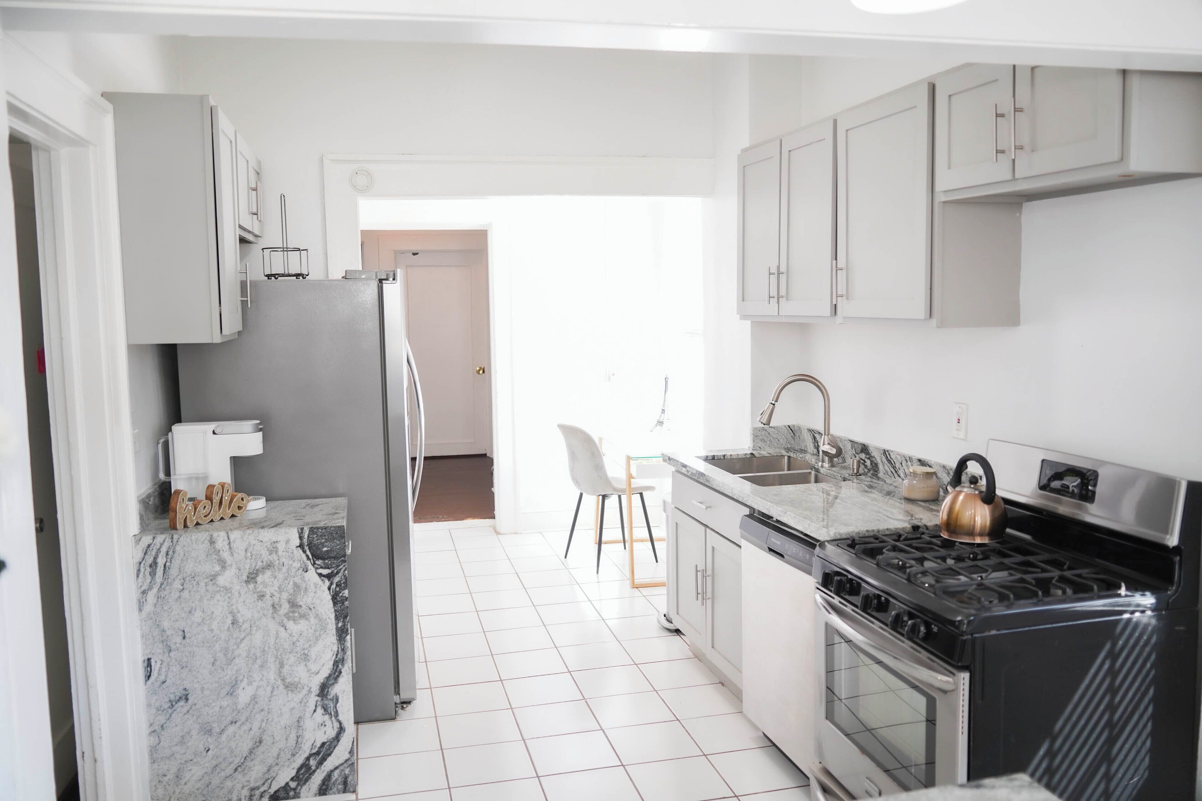 A kitchen with a refrigerator, stove, and sink, and a chair in the background.