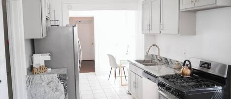 A kitchen with a refrigerator, stove, and sink, and a chair in the background.