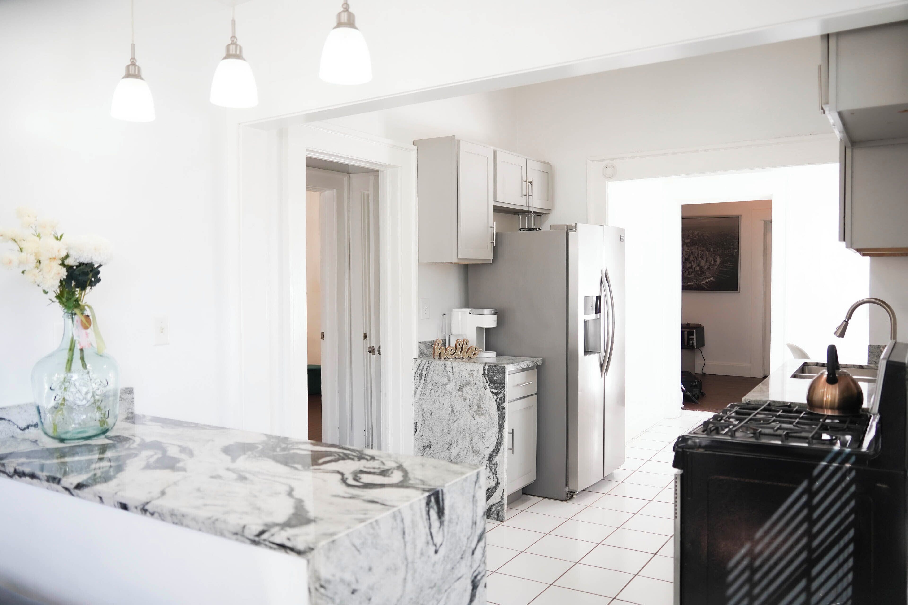 Une cuisine moderne avec des meubles blancs, un plan de travail en marbre, un réfrigérateur en acier inoxydable et une cuisinière à gaz.