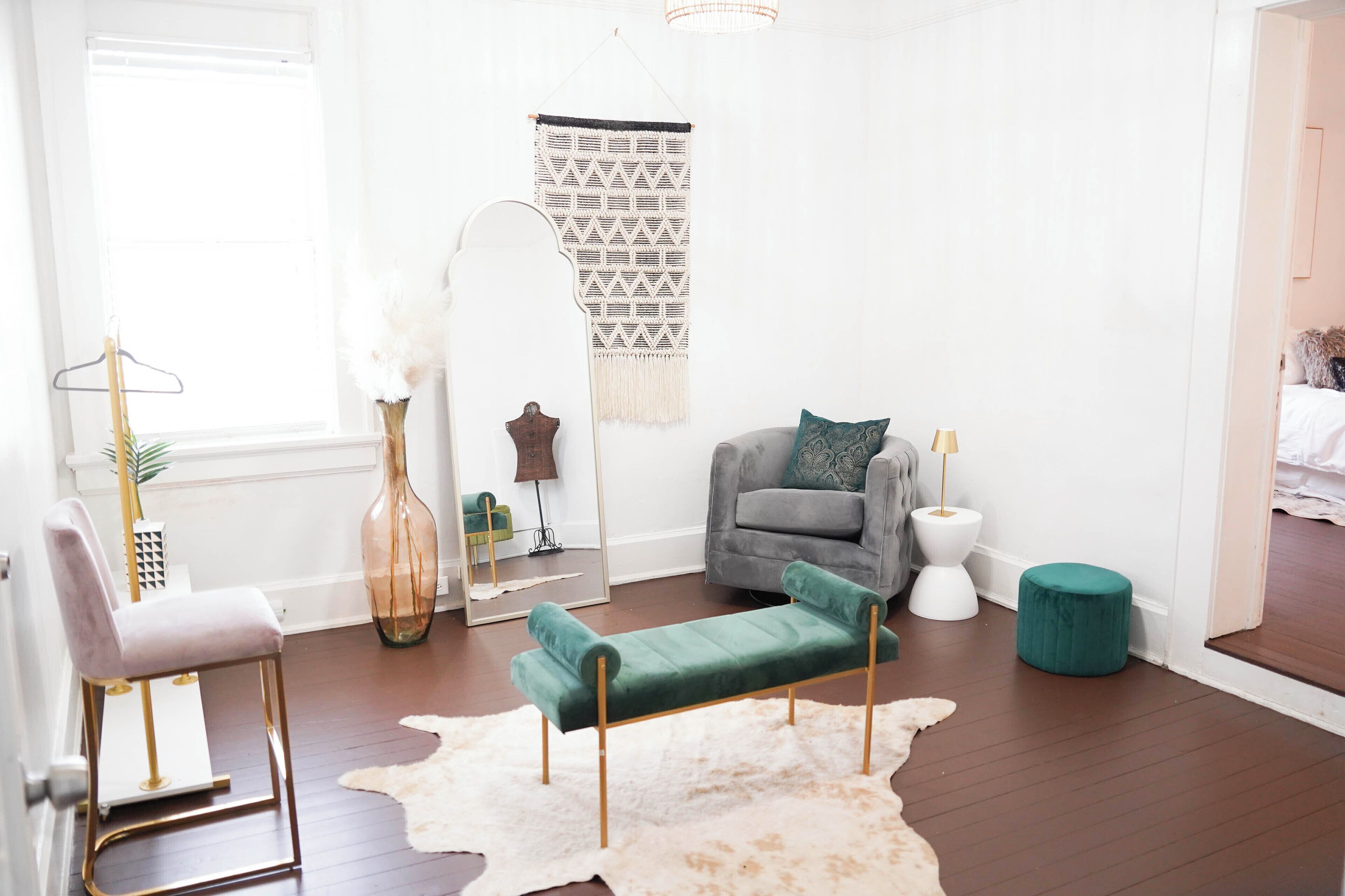 Una sala de estar moderna con un sofá gris, un banco verde, un tapete blanco y una decoración de macramé colgante en la pared.