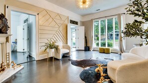 Un salon spacieux agrémenté d’un lustre moderne, d’une grande fenêtre avec des rideaux et d’un tapis en cuir.