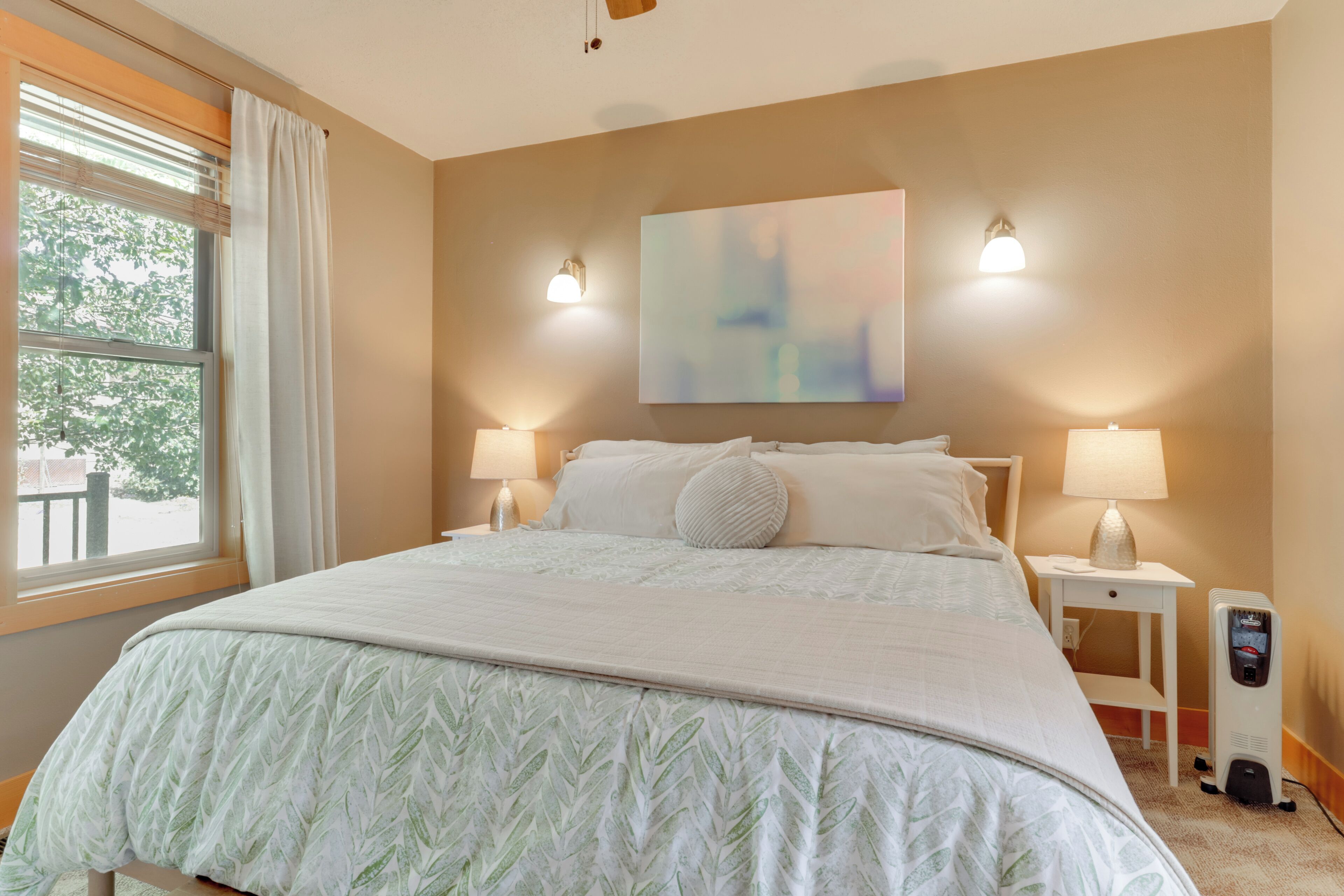 Quarto de hotel com uma cama grande, duas luminárias de cabeceira, um aquecedor e uma janela com cortinas.