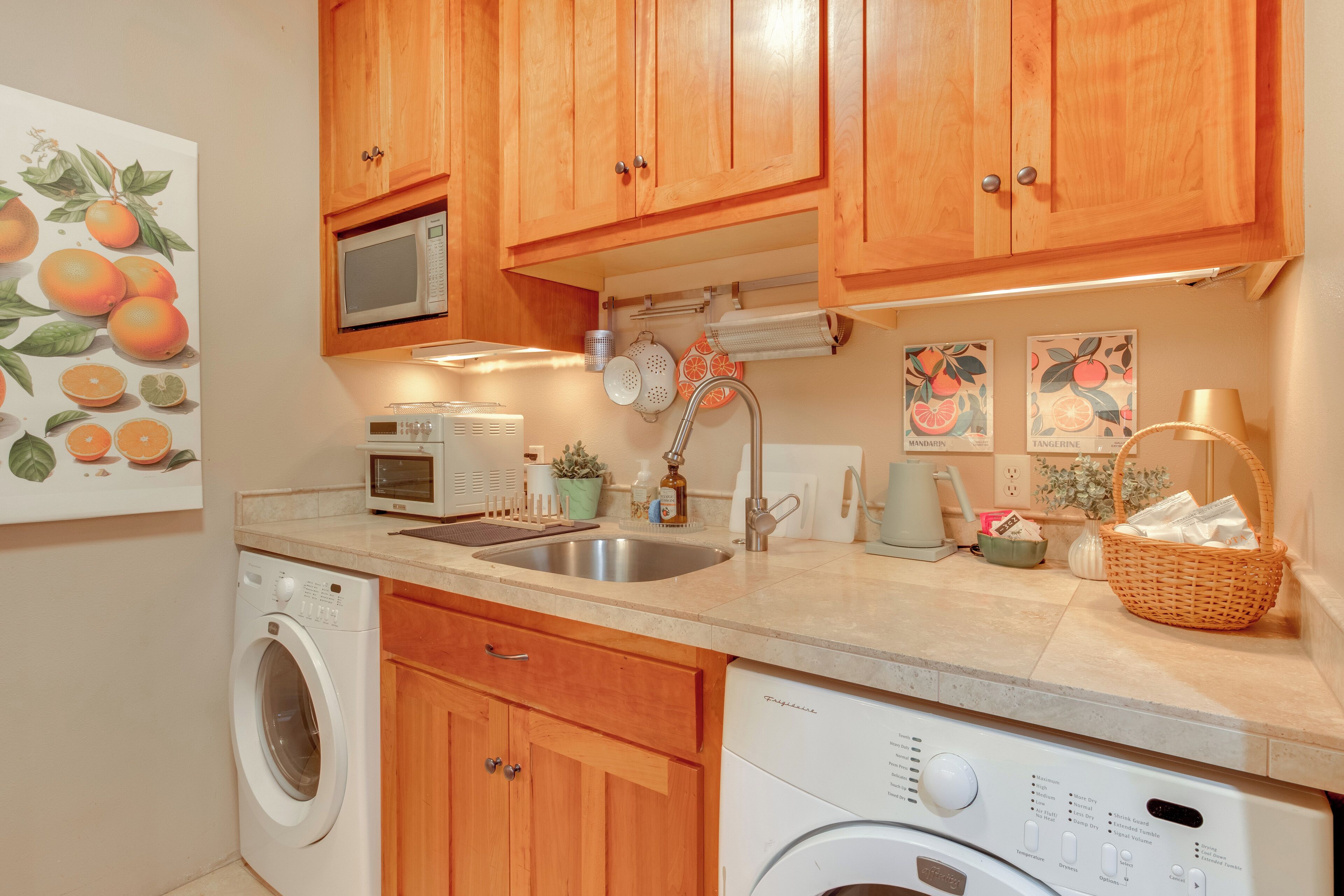 A kitchen with wooden cabinets, a washing machine, a microwave, and a sink.