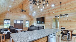 Une cuisine spacieuse dotée de plans de travail en granit, d’armoires en bois et d’un îlot central. On y trouve un coin repas avec une table et des chaises, ainsi qu’un coin salon avec un canapé et des fauteuils inclinables.