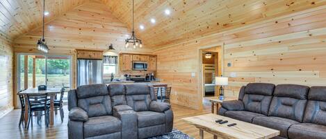 A spacious living area with a wooden ceiling, two sofas, a dining table, and a kitchen in the background.