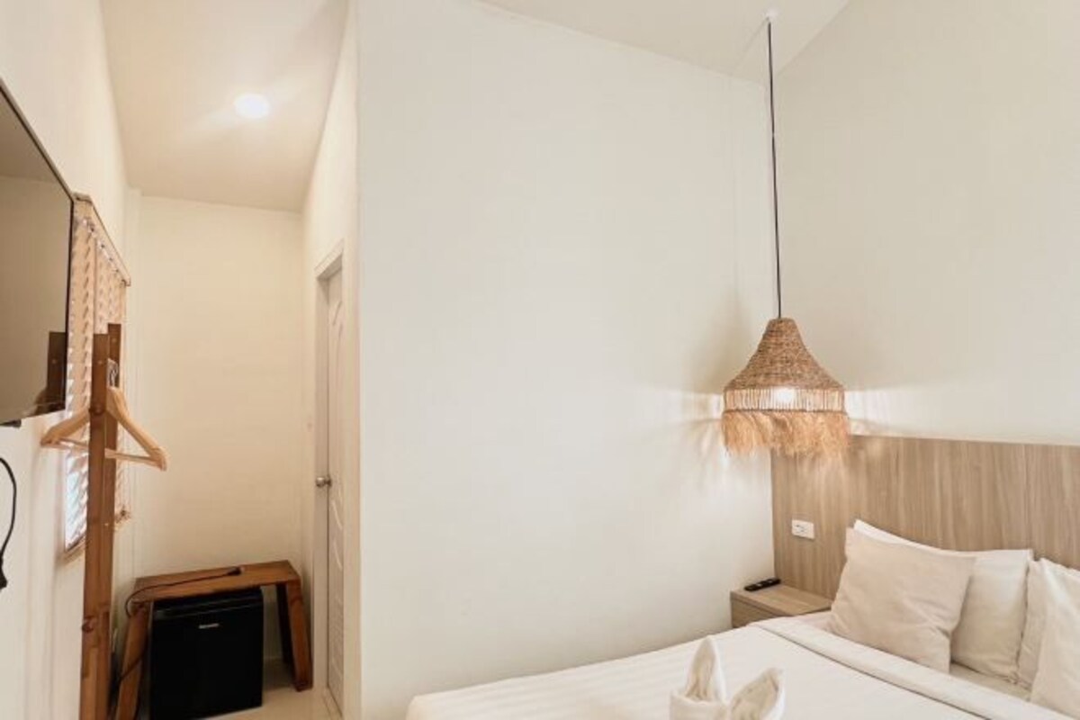 Hotellihuone, jossa on sänky, yöpöytä ja riippuvalaisin.