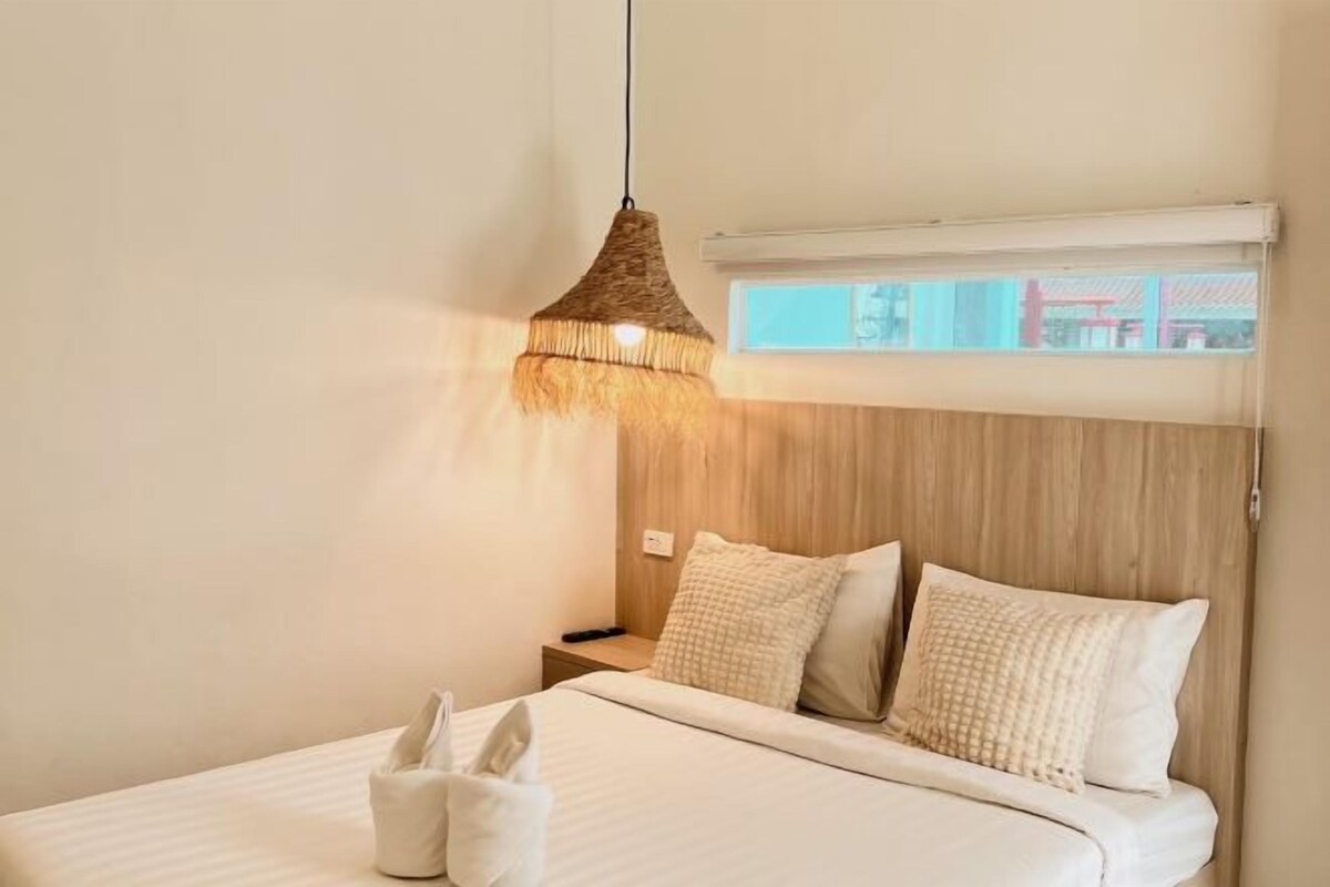 A bedroom with a bed, pillows, a nightstand, a lamp, and a window with a view.