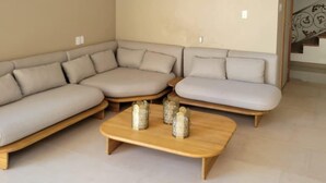 Un salon moderne avec un canapé d’angle, une table basse en bois et un escalier en arrière-plan.