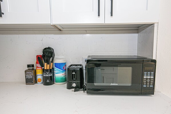 A kitchen counter with a microwave, a toaster, a container of black pepper, a can of cooking spray, and a bottle of oil. - Fun 3BR w/ Pool & Slide – Pet Friendly in San Jose (San Jose)