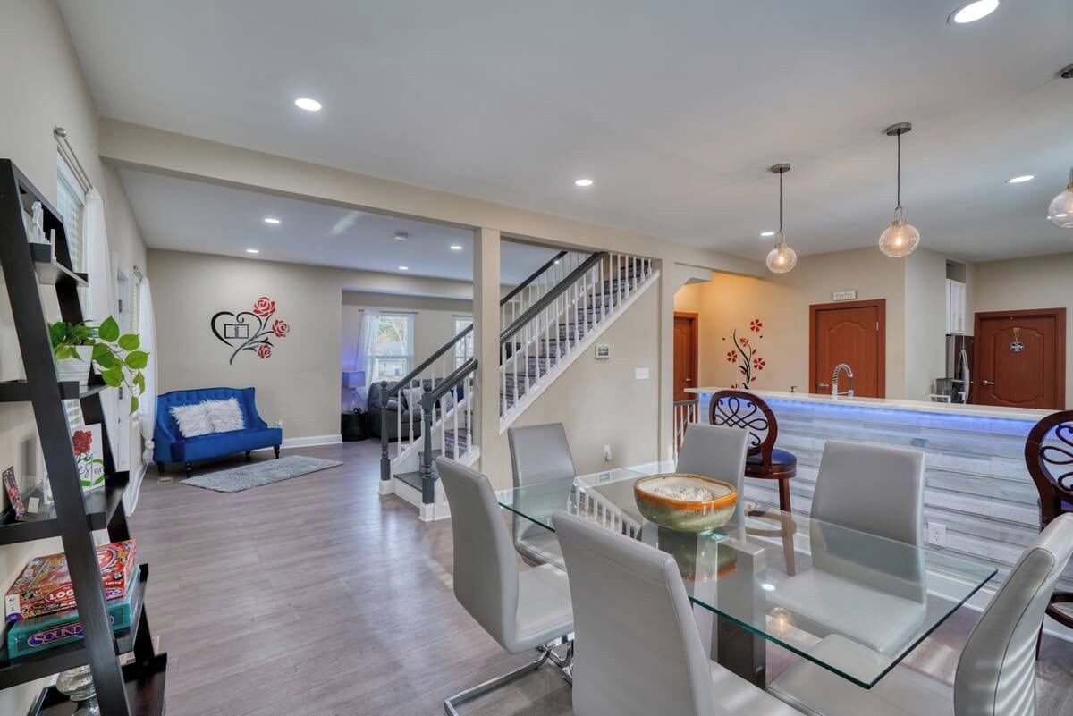 A modern living room with a glass dining table, white chairs, a blue sofa, and a staircase leading to another level.
