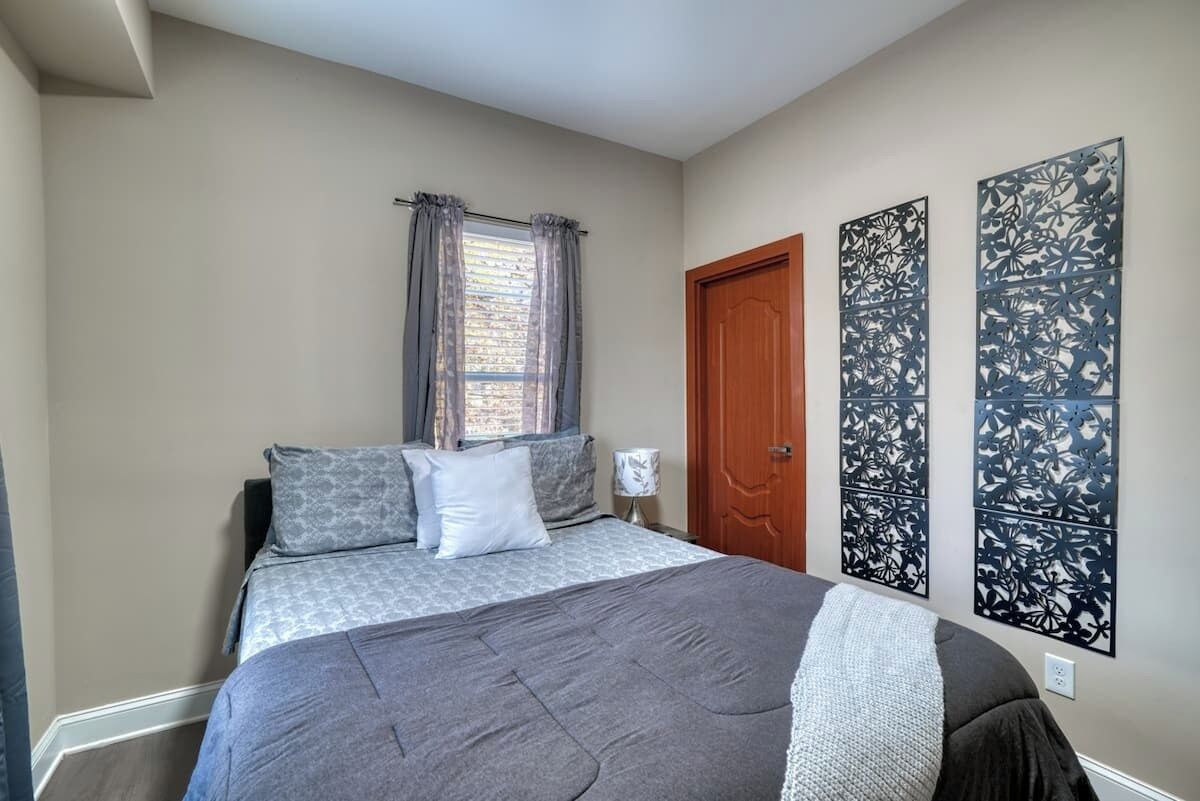A bedroom with a bed, curtains, a wooden door, and decorative wall panels.